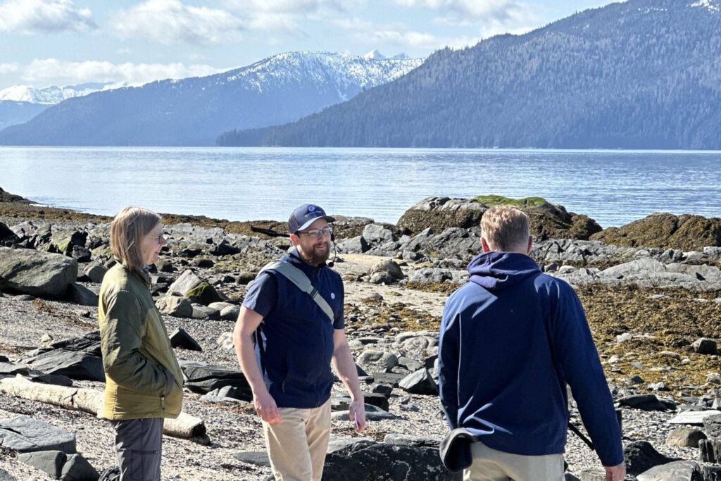 Tourists exploring Wrangell's Petroglyph Historic Beach shoreline with mountains in background.