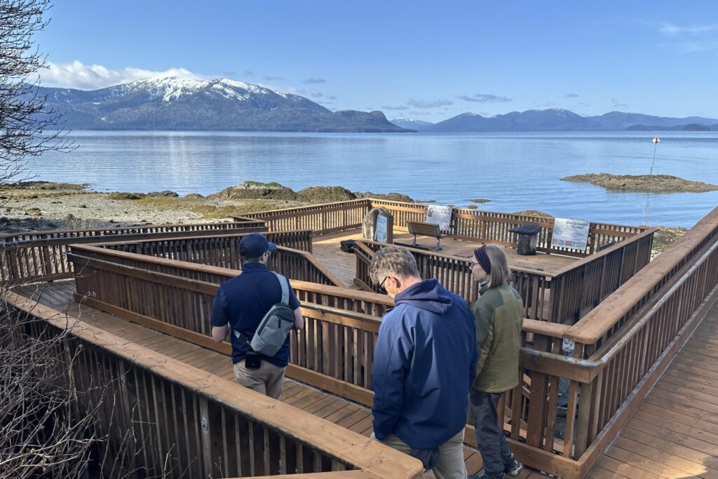 Tourists walking down the Petroglyph Historic Beach viewing deck with mountain and water views in Wrangell, Alaska.